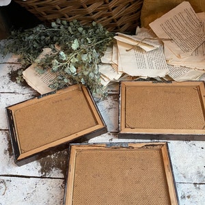 May include: Three brown picture frames with burlap backing. The frames are arranged on a white wooden surface.