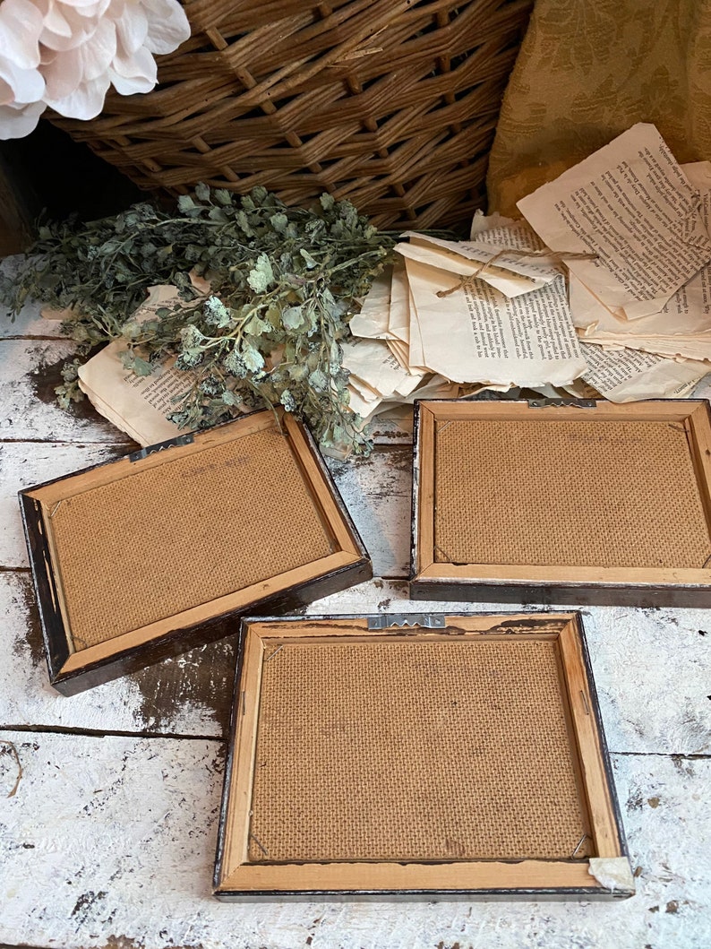 May include: Three brown picture frames with burlap backing. The frames are arranged on a white wooden surface.