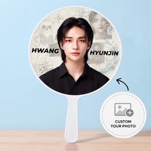 以下が含まれることがあります： 黒いシャツを着たダークヘアの人物のポートレートが描かれた、丸い白い手鏡。背景には「HWANG HYUNJIN」の文字、フェレットのイラスト、コンパスのデザインが含まれています。小さな円形のアイコンにはプラス記号とテキストが表示されています。