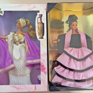 May include: Two collectible dolls in their original packaging. The left doll wears a white and purple gown with gold accents and a headpiece. The right doll wears a black bodice with a layered pink skirt and a black shawl, displayed in a gold box.