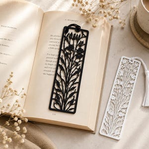 Puede incluir: Dos marcapáginas rectangulares con intrincados patrones florales y de enredaderas cortados con láser. Un marcapáginas es negro sólido con un cordón negro, y el otro es blanco sólido con una borla blanca a juego en el orificio superior.