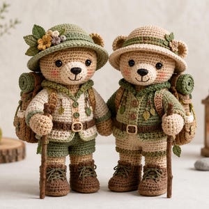Könnte beinhalten: Zwei gehäkelte Teddybären als Wanderer verkleidet, jeder trägt einen Hut mit kleinen Blumen, eine Jacke mit Knöpfen, Shorts und braune Stiefel. Sie tragen Rucksäcke mit aufgerollten Schlafsäcken und halten hölzerne Wanderstöcke in den Pfoten.