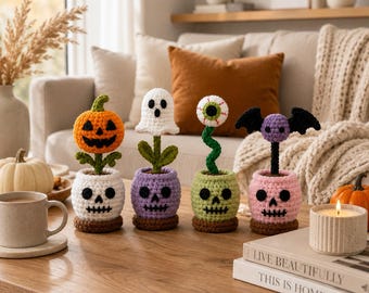 May include: Four crocheted Halloween decorations in skull-shaped pots. The first features an orange pumpkin, the second a white ghost, the third a green eyeball on a stem, and the fourth a purple bat. Each plant sits in a skull-shaped base.