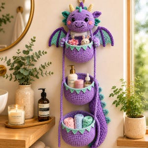 Peut inclure: Un organisateur mural en crochet violet en forme de dragon avec trois paniers superposés. La tête du dragon présente des cornes jaunes et des accents bleu sarcelle. Les paniers contiennent des petits objets, dont une figurine de lapin blanc.