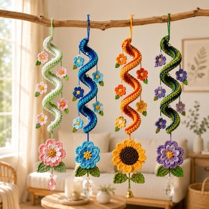 May include: Four hanging crochet spiral ornaments suspended from a wooden branch. Each spiral features small crocheted flowers, white beads, and a large bottom flower with green leaves. The ornaments include a pink, blue, orange, and purple color scheme.