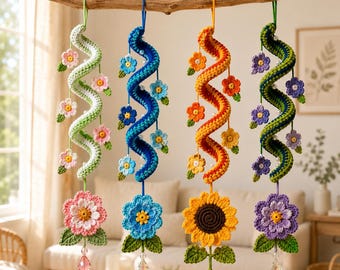 May include: Four hanging crochet spiral ornaments suspended from a wooden branch. Each spiral features small crocheted flowers, white beads, and a large bottom flower with green leaves. The ornaments include a pink, blue, orange, and purple color scheme.