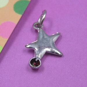 May include: A silver star charm with a red gemstone. The star has a five-pointed design and is attached to a loop for hanging.