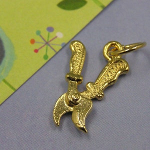 May include: Gold-toned metal charm shaped like a pair of pruning shears. The charm has a loop at the top for attaching to a bracelet or necklace.