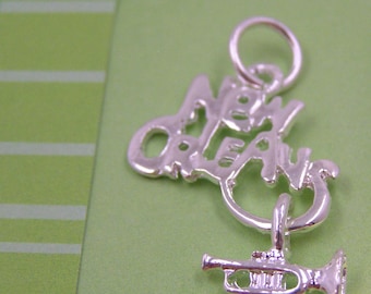 May include: Silver charm featuring the words "New Orleans" and a trumpet. The charm is designed to be attached to a bracelet or necklace.