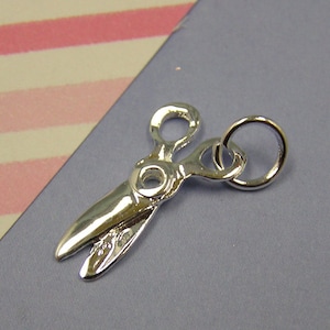 May include: A silver charm in the shape of a pair of scissors with a round jump ring.