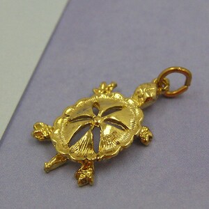 May include: Gold-toned turtle charm with a detailed cutout design. The charm has a loop for attaching to a necklace or bracelet.