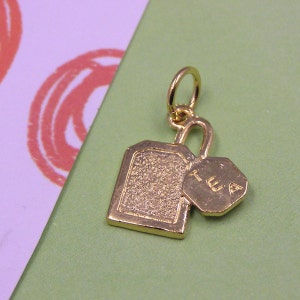 Puede incluir: Encanto de color dorado en forma de bolsita de té con la palabra "TEA" en un encanto más pequeño adjunto.