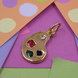 May include: Gold-tone charm shaped like a painter's palette with red, green, black, and clear rhinestones.