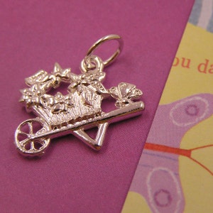 May include: Silver charm of a wheelbarrow filled with flowers and a butterfly on the side. The charm has a loop for attaching to a bracelet or necklace.
