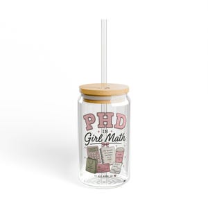 May include: A clear glass tumbler with a bamboo lid and a clear straw. The glass features the pink and black text "PHD IN Girl Math" above illustrations of a calculator, a notebook, a coffee cup, a shopping bag, a credit card, and a receipt.