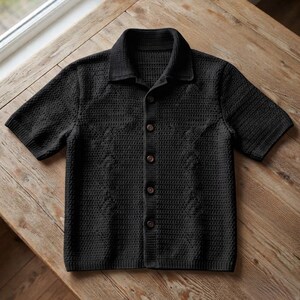 Peut inclure: Une chemise noire à manches courtes avec un motif en maille gaufrée texturée. Le vêtement présente un col classique, une patte de boutonnage avant avec cinq boutons foncés, ainsi que des finitions côtelées aux poignets et à la base.