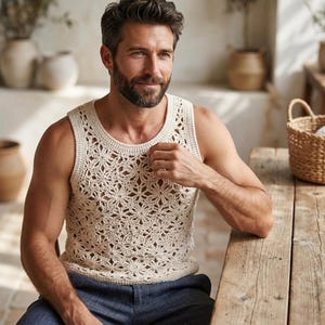 Puede incluir: Una camiseta sin mangas de ganchillo en color crema con un intrincado patrón floral repetitivo en toda la prenda. La parte superior tiene un cuello redondo y está confeccionada con un delicado tejido de punto calado con textura.