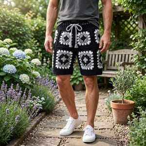 May include: Crochet shorts featuring a black, white, and gray granny square pattern with a drawstring waist. The shorts are paired with a plain gray t-shirt and white sneakers, showcasing a detailed textile design with visible yarn stitching.