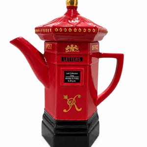 Könnte beinhalten: Eine rot-schwarze Keramik-Teekanne in Form eines britischen Briefkastens. Sie verfügt über einen goldenen Knauf, einen Ausguss, einen Henkel und den Text POST OFFICE, LETTERS sowie Last Collection Time Monday to Friday 5.30 p.m. Ein goldenes Emblem ist aufgedruckt.