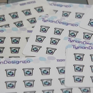 May include: A sheet of white sticker paper with multiple blue and purple recycling bin icons. The paper has the text "TyrianDesign.co" printed on it.