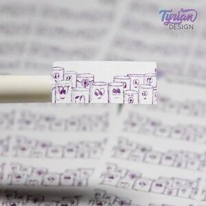 Puede incluir: Una pegatina blanca con una ilustración morada de cilindros de dibujos animados con caras. La pegatina está sobre un bolígrafo blanco. El texto "Tyrian DESIGN" está en la esquina superior derecha.