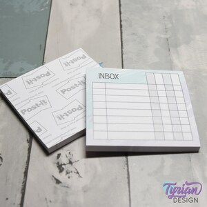 Op de afbeelding: Twee vierkante Post-it-notitieblokken. Eén blok is open en toont het woord "INBOX" bovenaan, met een raster van lijnen eronder. Het andere blok is gesloten en toont het Post-it-logo. De achtergrond is een lichtgrijze en blauwe houtnerf.