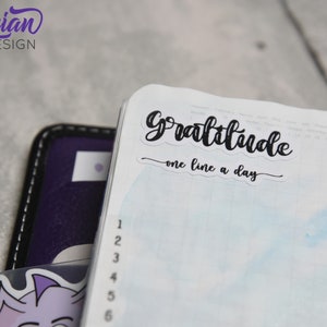 May include: A white planner with a blue watercolor background. A black sticker with the text "Gratitude - one line a day" is on the top of the page.