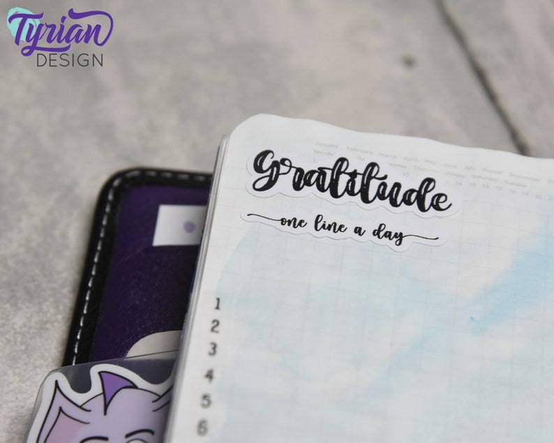 May include: A white planner with a blue watercolor background. A black sticker with the text "Gratitude - one line a day" is on the top of the page.