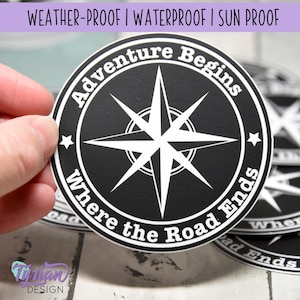 May include: Black and white round sticker with a compass rose and the text "Adventure Begins Where the Road Ends".