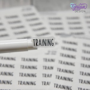 May include: A close-up of a white sticker with the word "TRAINING" printed in black. The sticker is being held by a white marker.