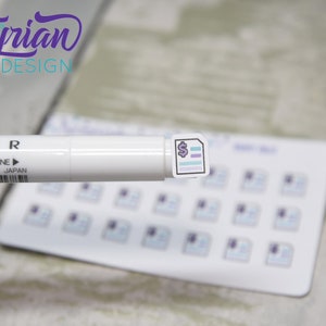 May include: A sheet of stickers with a purple and blue design of a document with a dollar sign. The stickers are on a white background. A white marker is in the foreground.