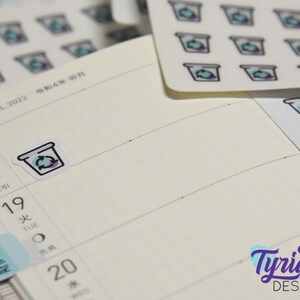 May include: A sheet of stickers with a design of a coffee cup with a recycling symbol. The stickers are white with a light blue and purple design. The stickers are on a white background.