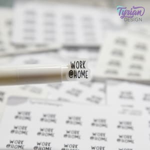 May include: A sheet of white stickers with the text "WORK @HOME" printed on them. The stickers are being held by a white pen.