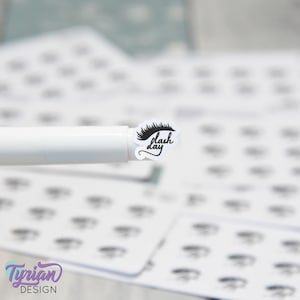 May include: A white sticker with a black eyelash design and the text "lash day" in black script.