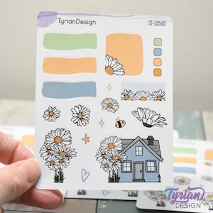 May include: A sheet of planner stickers featuring daisies, a blue house, and various shapes in pastel colors. The stickers include a bee, stars, and the text "TyrianDesign" and "ST-10582".