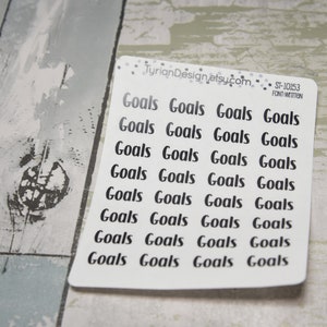 May include: A white sticker sheet with the word "Goals" printed in a black handwritten font. The sticker sheet has the text "TyrianDesign.etsy.com" and "ST-10153 FONT-WITTEN" printed on it. The sticker sheet is on a light gray and white wooden surface.