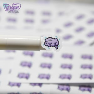 Pode incluir: Uma folha de adesivos com um design de cérebro roxo. O cérebro tem um contorno azul claro e brilhos. Os adesivos estão sobre um fundo branco.