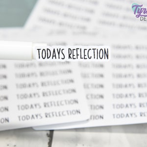 Może przedstawiać: Biała naklejka z tekstem "TODAYS REFLECTION" czarnymi literami. Naklejka znajduje się na stosie podobnych naklejek.