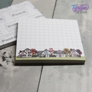 May include: A white notepad with a grid pattern and a green bottom border. The bottom border features a row of houses with colorful flowers and greenery.