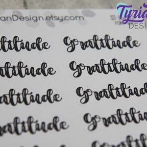 May include: A sheet of stickers with the word "Gratitude" written in black cursive lettering. The stickers are on a white background.