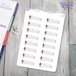 Puede incluir: Una hoja de pegatinas con fondo blanco. Cada pegatina presenta un icono de gota de sangre roja sobre un gráfico para controlar los niveles de azúcar en sangre. El gráfico incluye espacios para lecturas AM y PM, y los días de la semana.