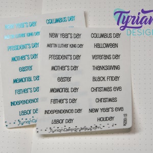 May include: Two sheets of clear stickers with various holiday names printed in black and blue. The stickers include holidays such as New Year's Day, Columbus Day, Martin Luther King Day, President's Day, Mother's Day, Easter, Memorial Day, Father's Day, Independence Day, Labor Day, Halloween, Veterans Day, Thanksgiving, Black Friday, Christmas Eve, Christmas, New Year's Eve, and Holiday.