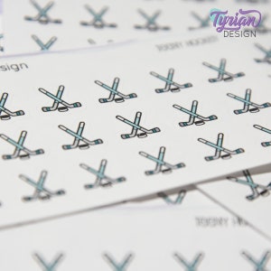 Pu&ograve; includere: Un foglio di carta adesiva bianca con pi&ugrave; adesivi di bastone da hockey e disco. Gli adesivi sono neri e blu con un contorno bianco. Il testo "Tyrian Design" &egrave; nell'angolo in alto a destra del foglio.