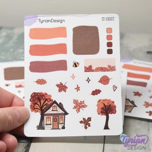Pode incluir: Uma folha de autocolantes com tema de outono com vários desenhos. Os autocolantes incluem amostras de cores, uma abelha, folhas, estrelas, uma casa e árvores. A paleta de cores apresenta tons de laranja, castanho e bordô. O texto "TyrianDesign" e "ST-10022" são visíveis.