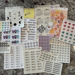 May include: A collection of planner stickers featuring various designs, including moon phases, calendars, and icons. The stickers are in various colors and sizes, with text such as "Canceled" and "Rescheduled". There is also a yellow sticky note with the number "101".