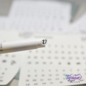 May include: A white marker with a round, white sticker on the end. The sticker has the number 27 printed on it in black.