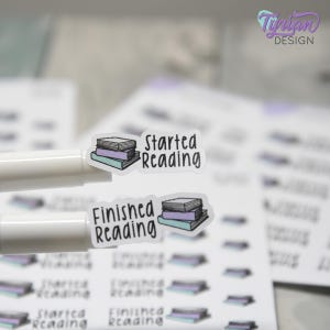 May include: Clear stickers with a stack of books and the phrases "Started Reading" and "Finished Reading" in black. The books are in shades of gray, purple, and blue. The stickers are on a white background.