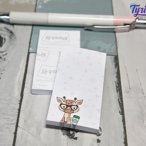 May include: A white notepad with a light blue background and a cartoon giraffe wearing glasses and holding a cup of coffee. The notepad has the text "Post-it" printed on it.