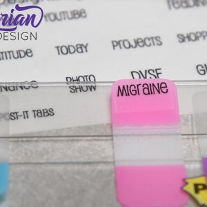 K&ouml;nnte beinhalten: Ein rosa Haftnotiz mit dem Wort "Migraine" in schwarzer Schrift. Der Notiz ist an einem durchsichtigen Plastikteiler mit anderen Haftnotizen in verschiedenen Farben befestigt.