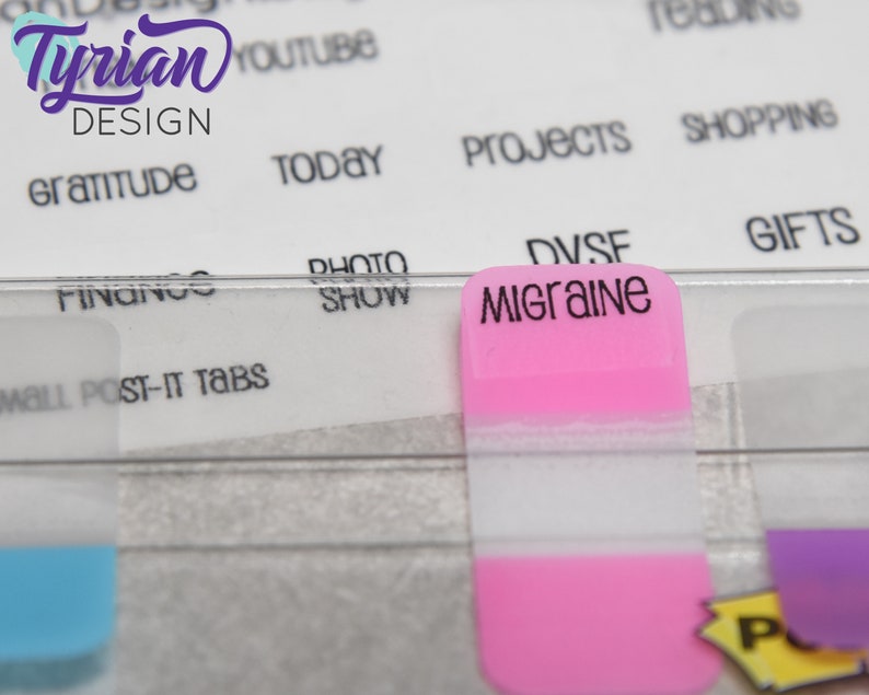 K&ouml;nnte beinhalten: Ein rosa Haftnotiz mit dem Wort "Migraine" in schwarzer Schrift. Der Notiz ist an einem durchsichtigen Plastikteiler mit anderen Haftnotizen in verschiedenen Farben befestigt.
